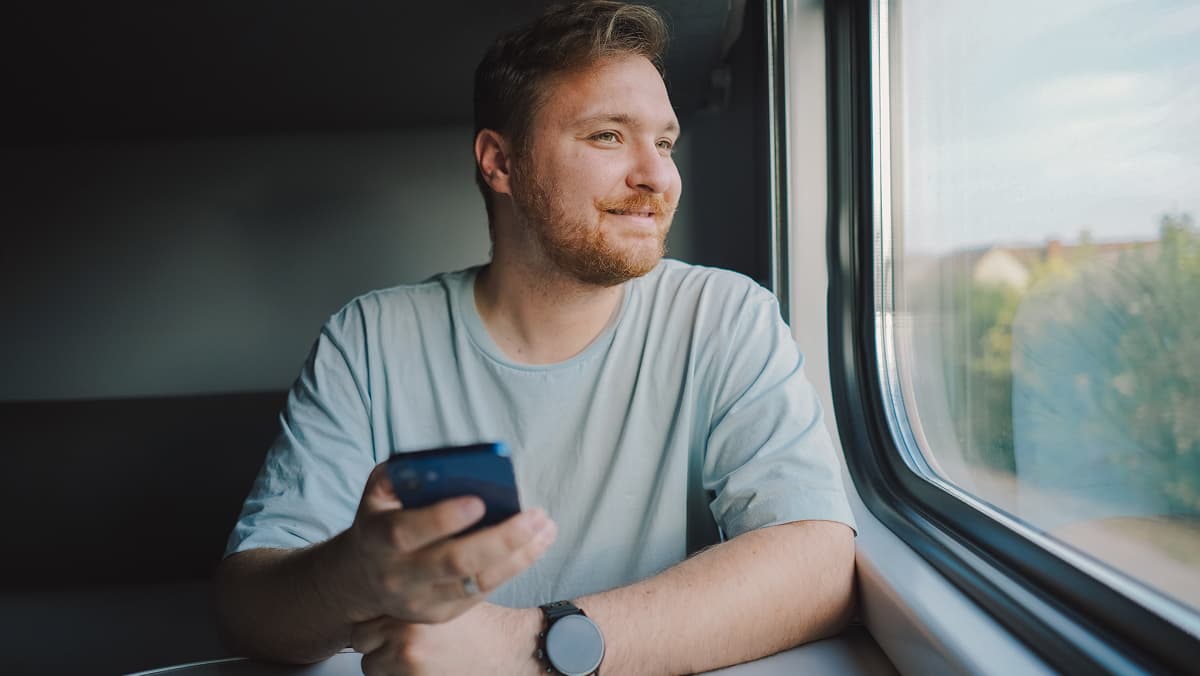 Mann schaut aus Zugfenster und hat Smartphone in rechter Hand